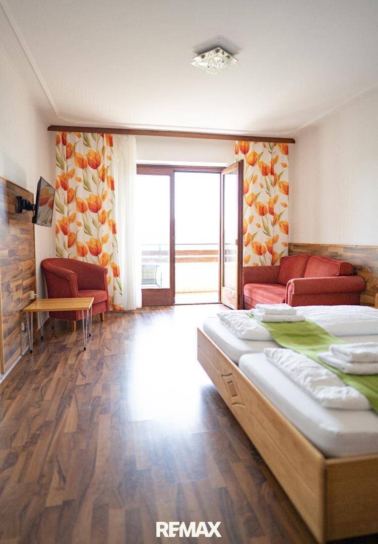 Schlafzimmer mit Bett, Sofa, Fernseher und Zugang zu einem Balkon, hell und komfortabel.