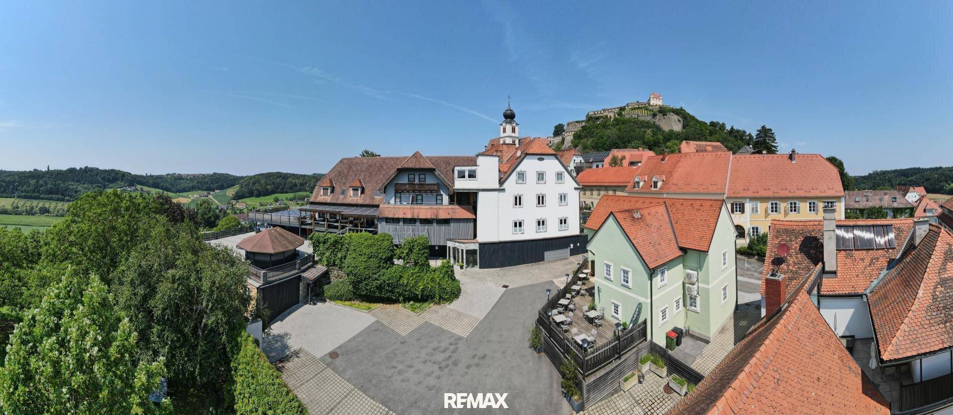 Panoramablick auf ein malerisches Dorf mit historischen Gebäuden und einer Burg auf einem Hügel im Hintergrund.