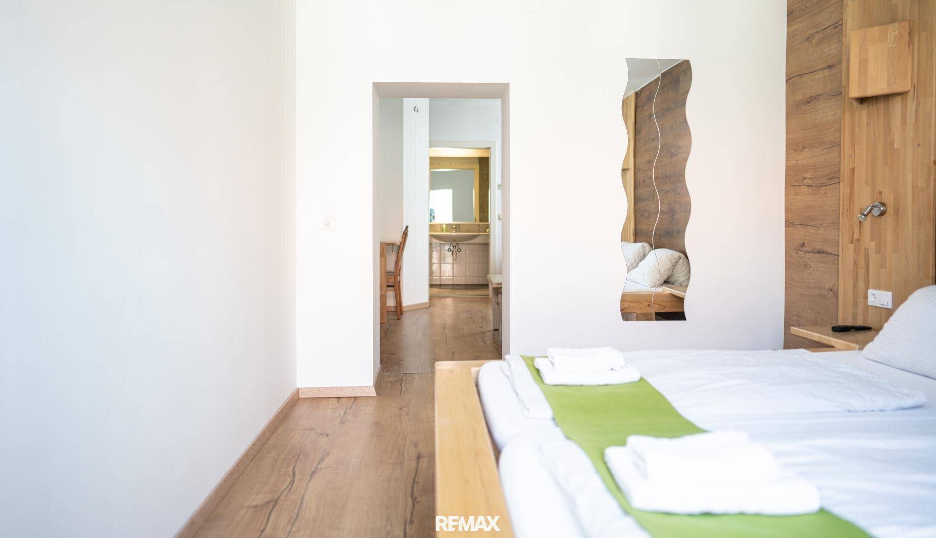 Schlafzimmer mit Holzwandvertäfelung und Blick in ein angrenzendes Badezimmer, hell und offen.