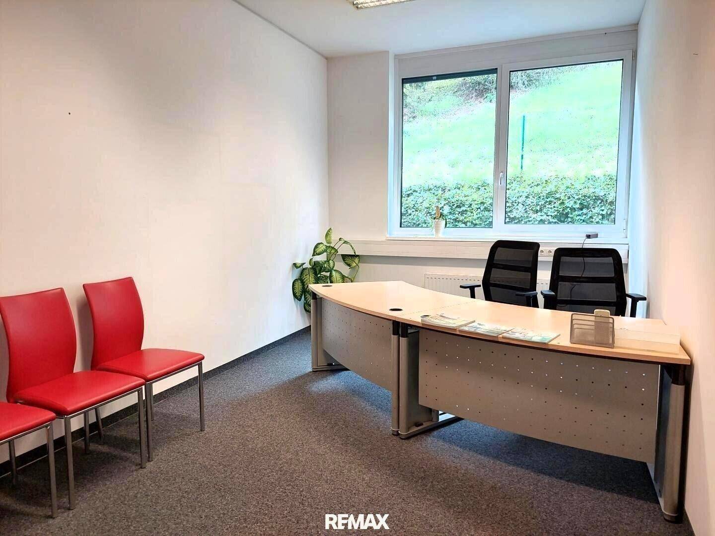 Einzelbüro mit Schreibtisch, Bürostühlen und einem großen Fenster mit Blick ins Grüne.