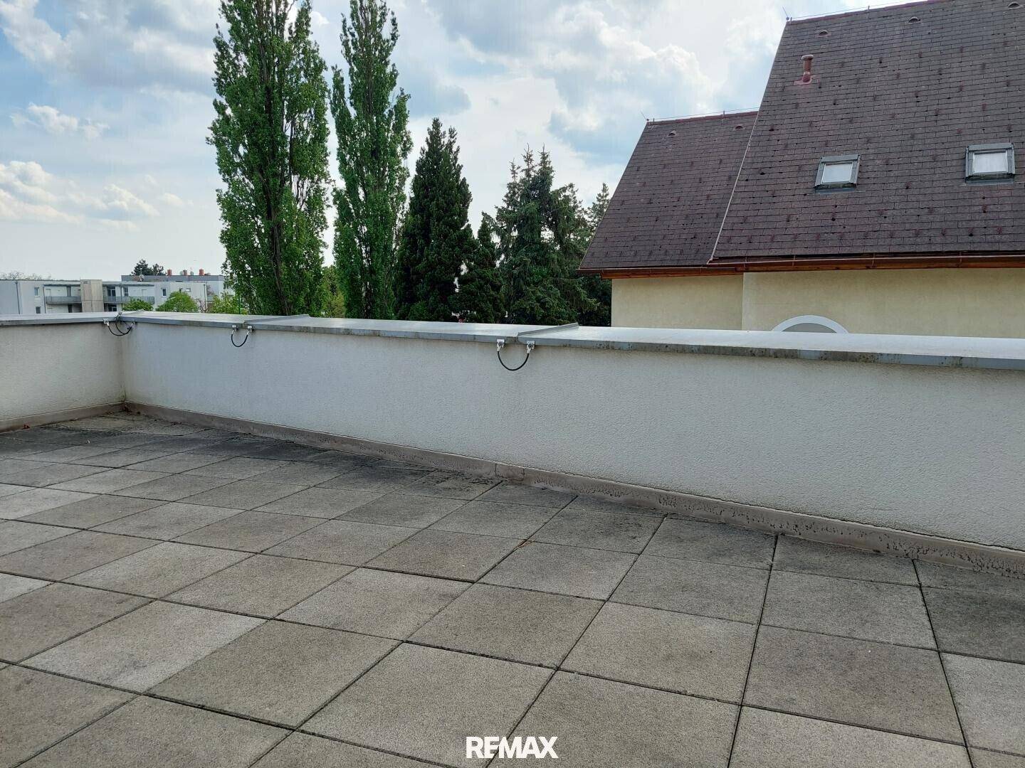 Weitläufige Dachterrasse mit Blick auf die Umgebung und das Dach eines benachbarten Gebäudes.
