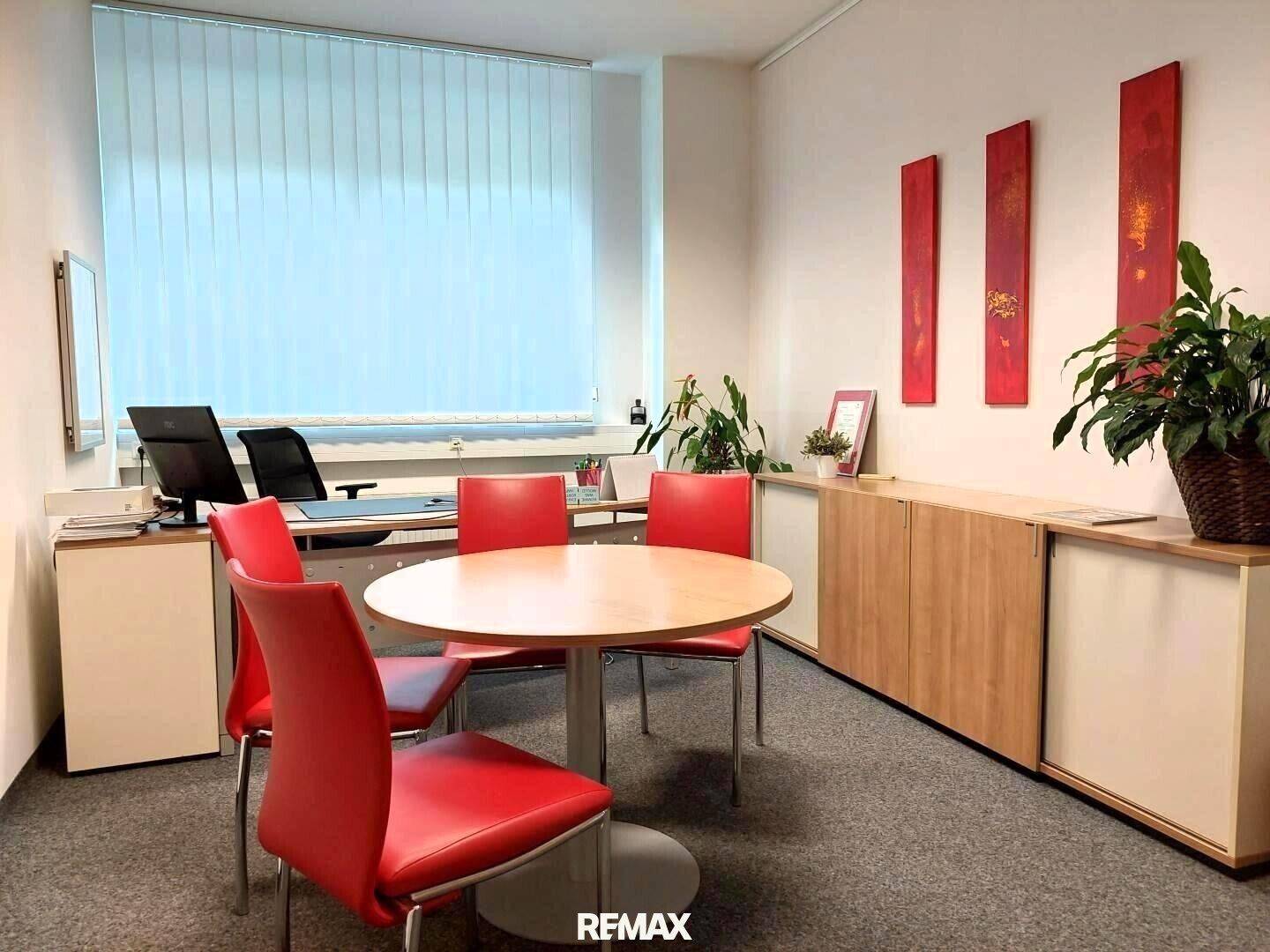 Modernes Büro mit Teppichboden, einem runden Besprechungstisch und Schränken entlang der Wand.
