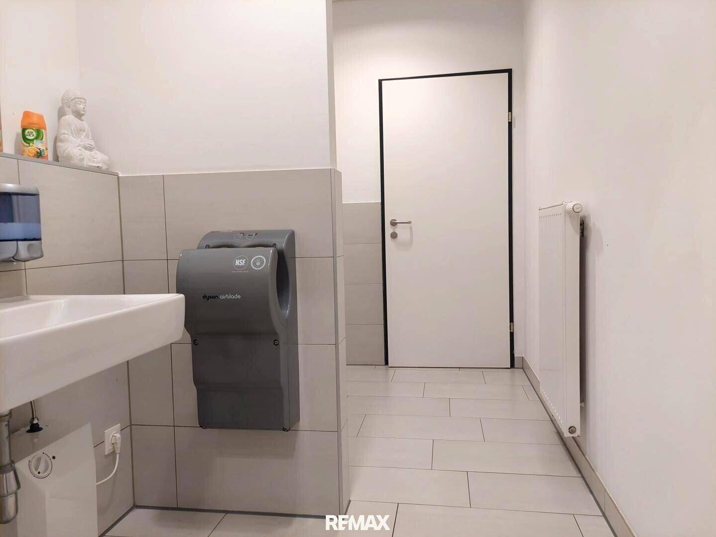 Helle Toilette mit Fliesenboden, Handwaschbecken und einem Heizkörper unter dem Fenster.