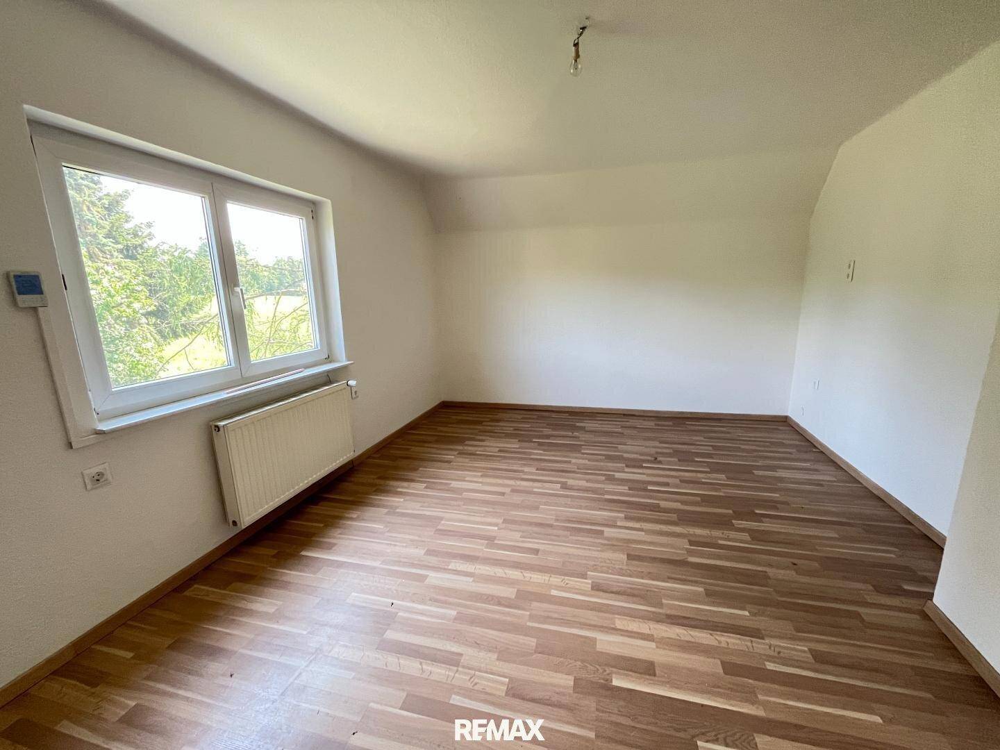 Helles Schlafzimmer im Dachgeschoss mit Laminatboden, Fenster und Blick auf die Natur.