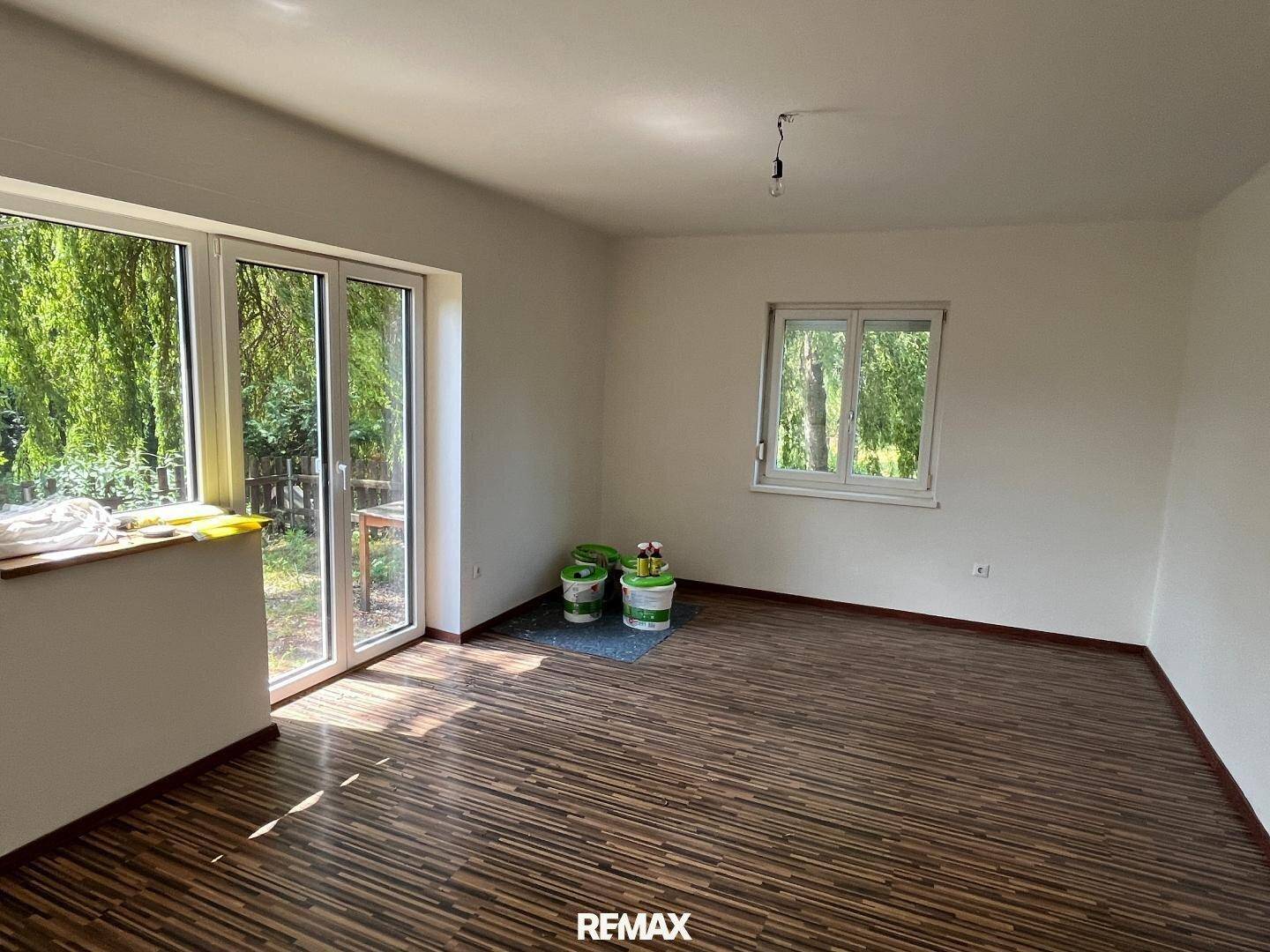 Geräumiges Wohnzimmer mit Laminatboden, großen Fenstern und direktem Zugang zum Garten.