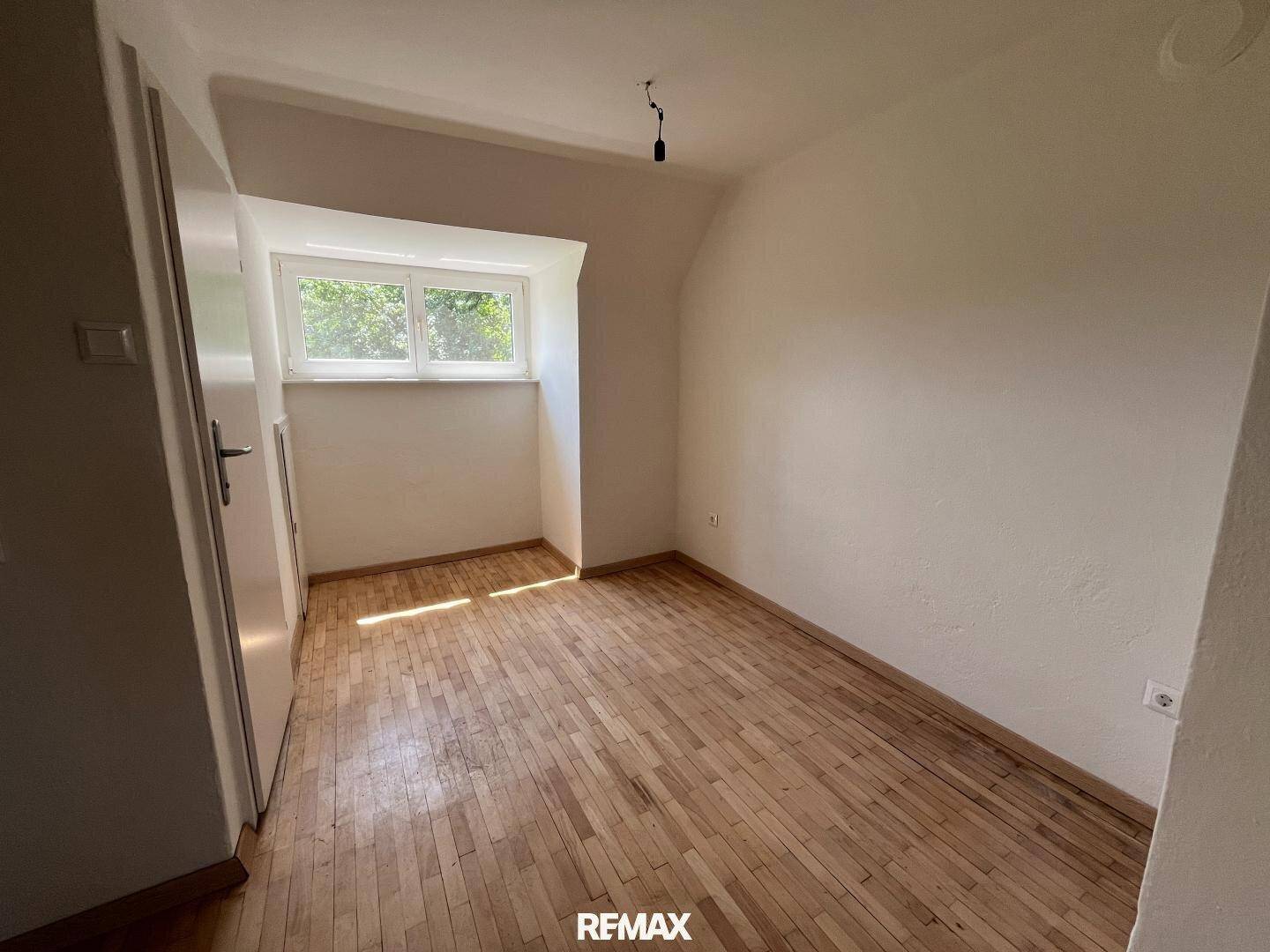 Helles Schlafzimmer im Dachgeschoss mit Holzboden, Fenster und schrägen Wänden.