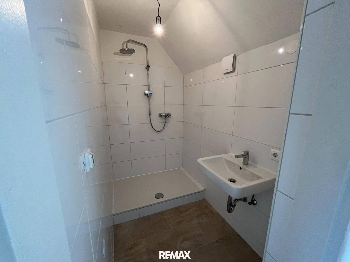 Modernes Badezimmer im Dachgeschoss mit Dusche, Waschbecken und weißen Fliesen.