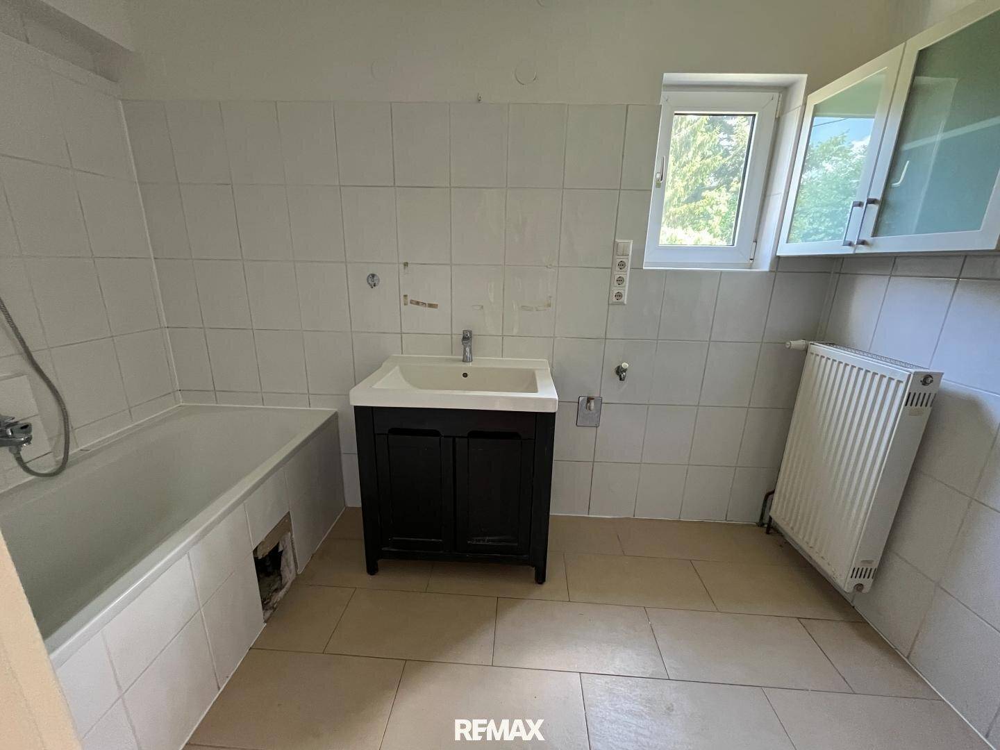Einfaches Badezimmer mit Badewanne, Waschbecken und Fenster, bereit zur Renovierung.