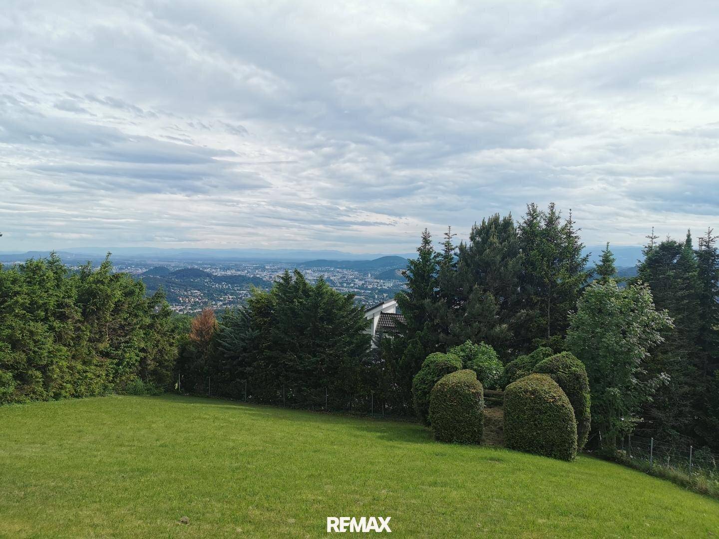 Weitläufiges Grundstück mit grüner Wiese, Bäumen und Panoramablick auf die Stadt.