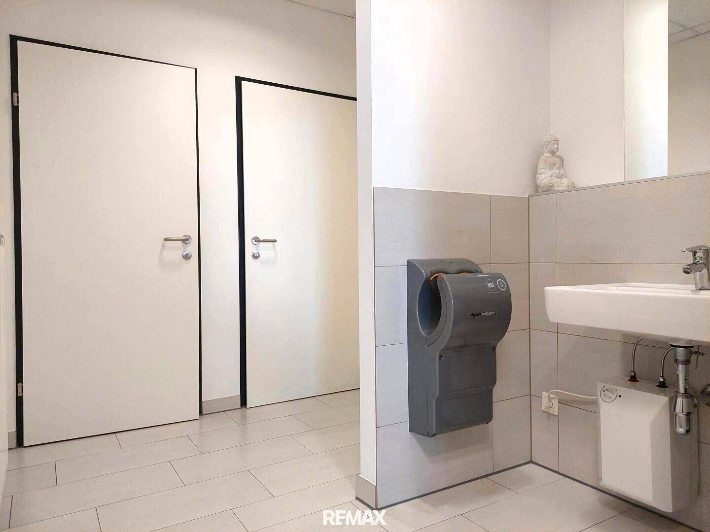 Heller Waschraum mit modernem Handtrockner, Waschbecken und zwei weißen Türen.