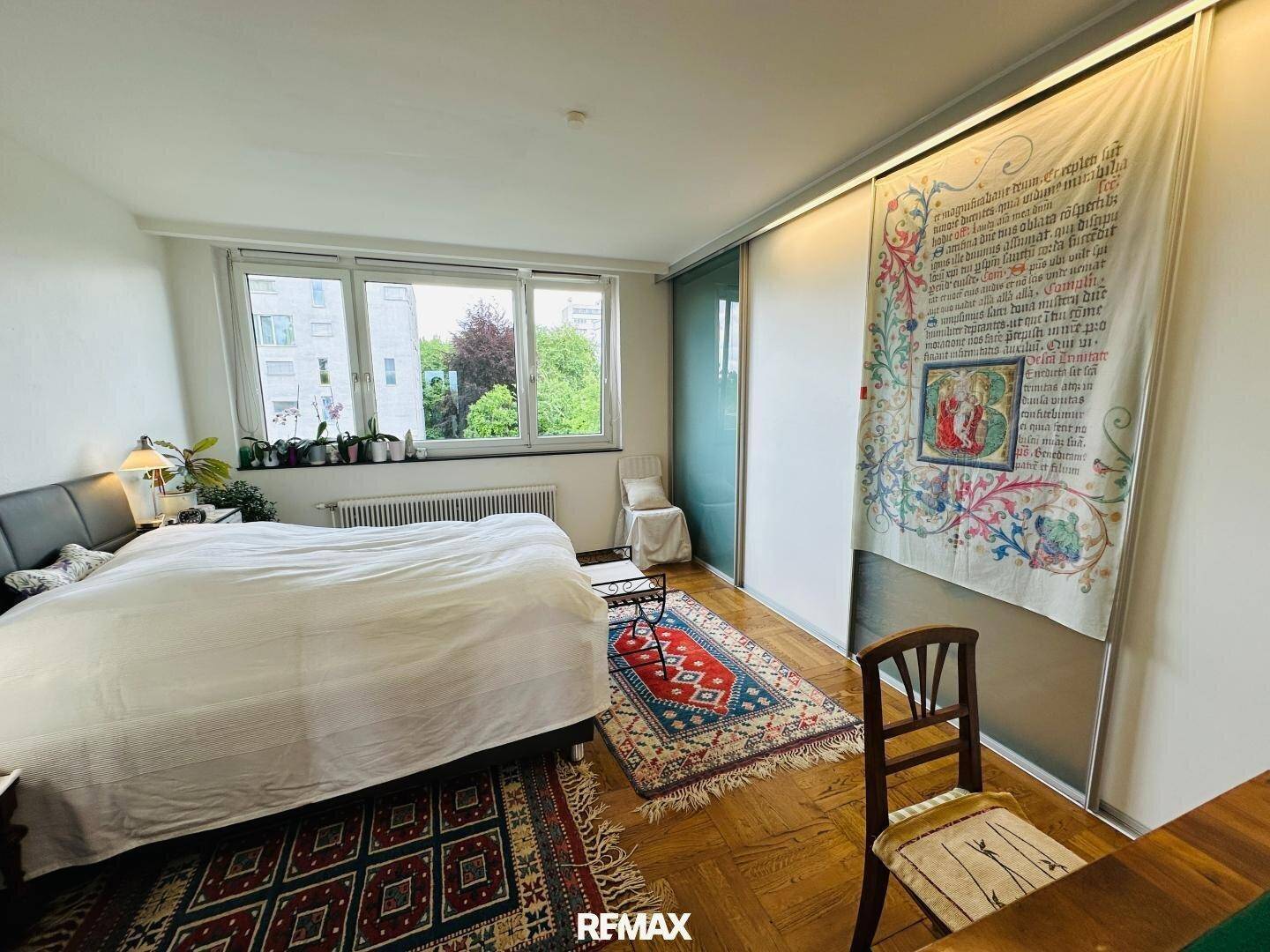 Schlafzimmer mit großem Bett, Holzparkett und Fenster mit Blick ins Grüne.