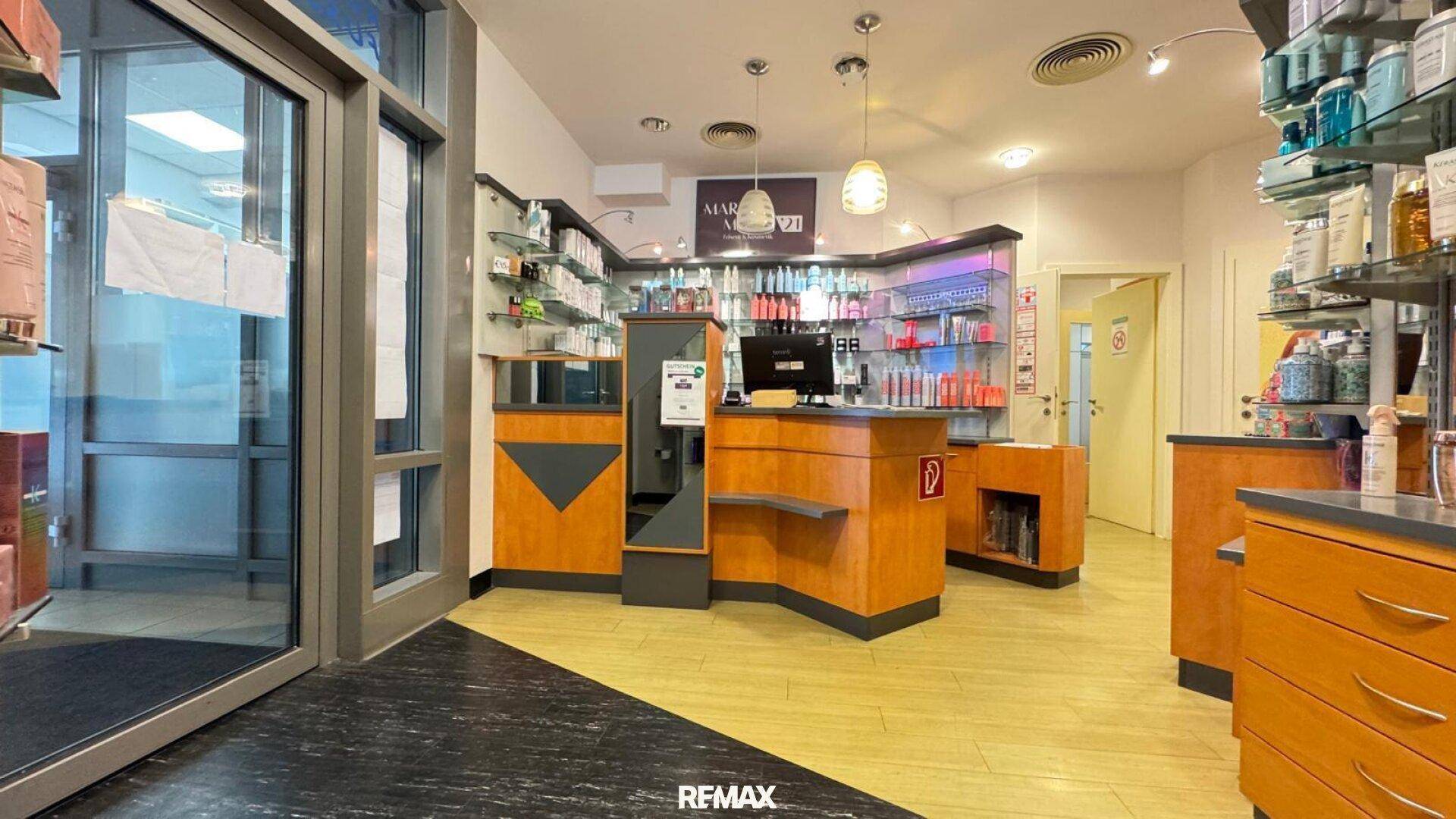 Empfangsbereich eines Salons mit Verkaufstheke, Produktregalen und gemischtem Bodenbelag.
