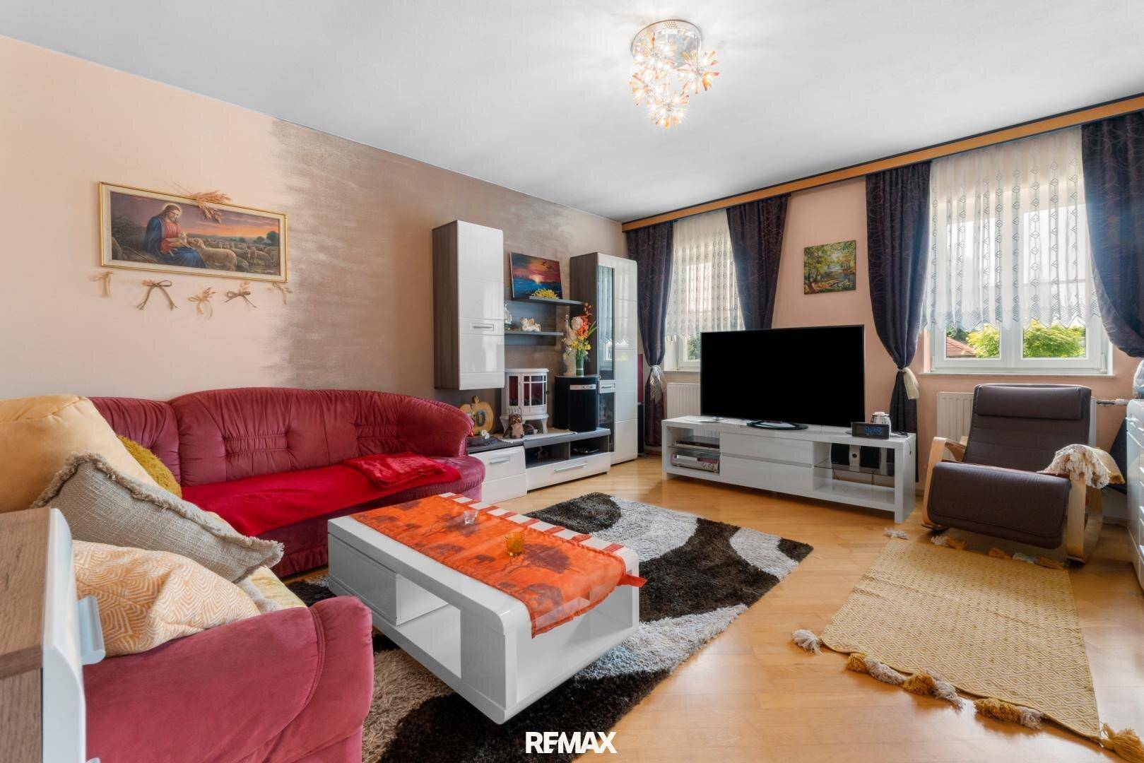 Geräumiges Wohnzimmer mit bequemen Sofas, Fernseher und Blick auf den Garten durch die Fenster.