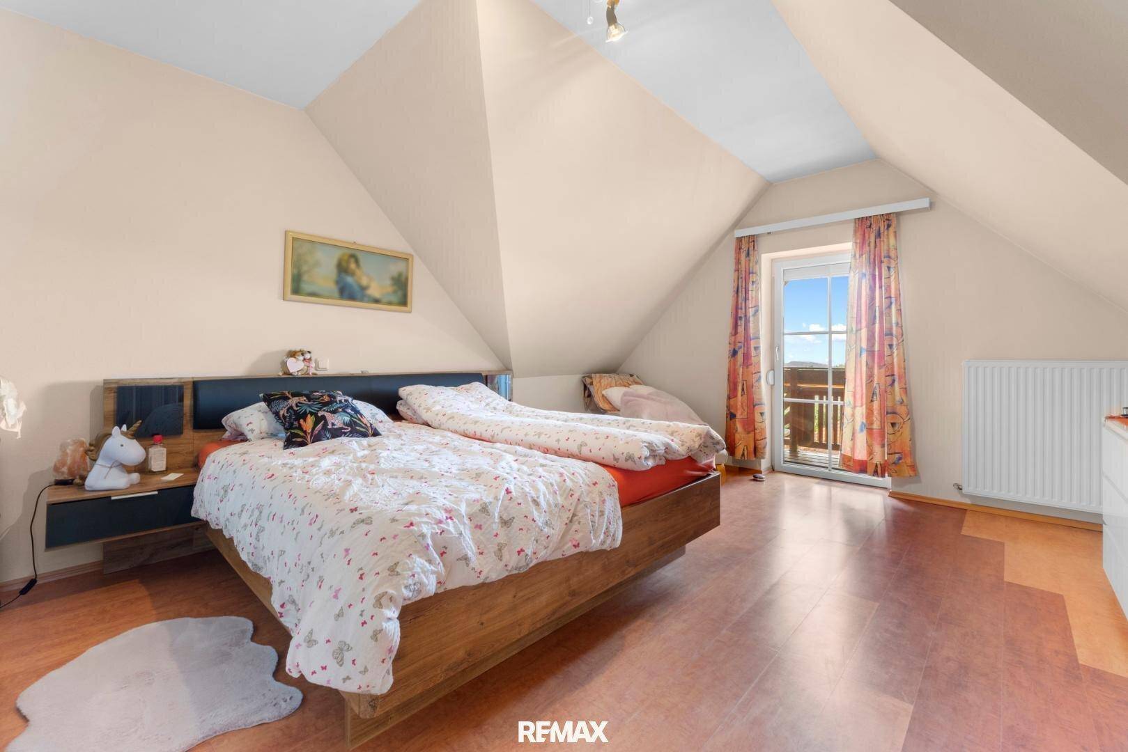 Gemütliches Schlafzimmer im Dachgeschoss mit Dachschrägen, Holzbett und Zugang zum Balkon.