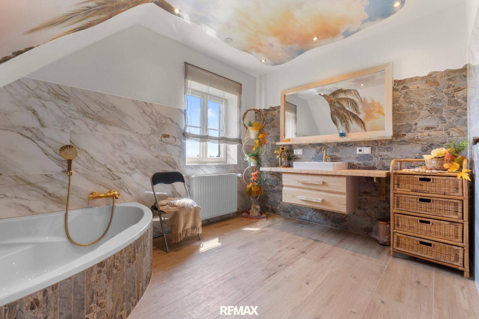 Großes Badezimmer mit Badewanne, Waschtisch und dekorativen Stein- und Marmorfliesen.