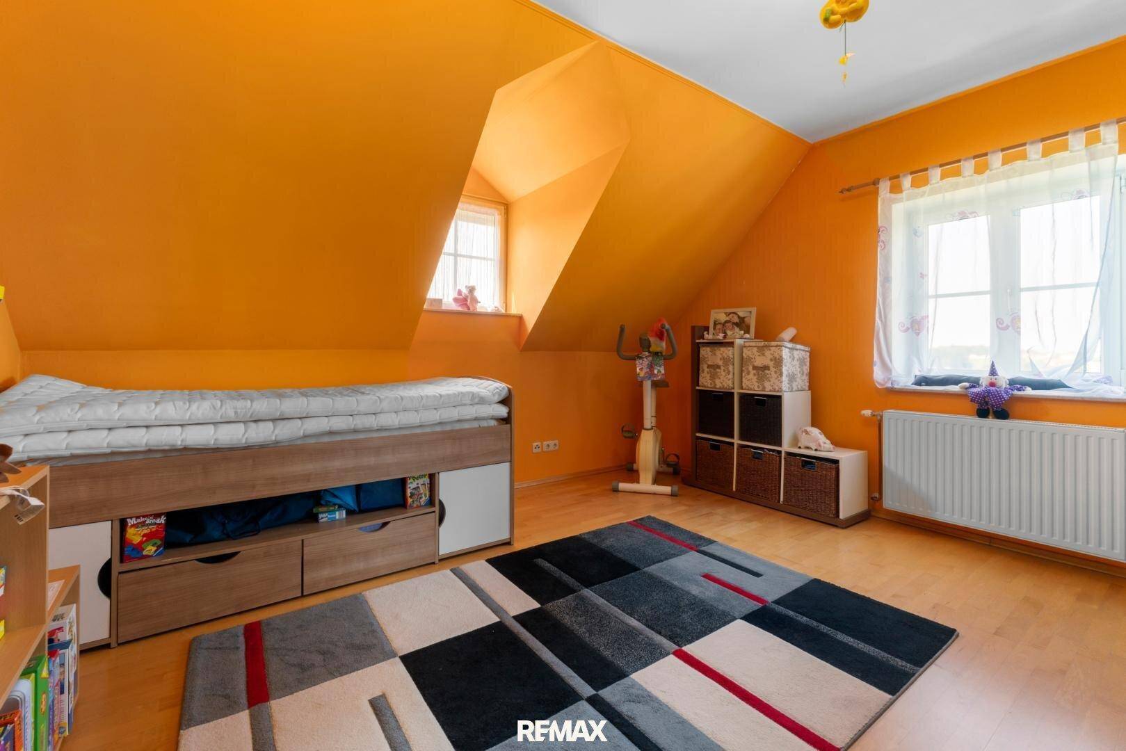 Helles Kinderzimmer mit orangefarbenen Wänden, Dachschrägen und Holzboden.