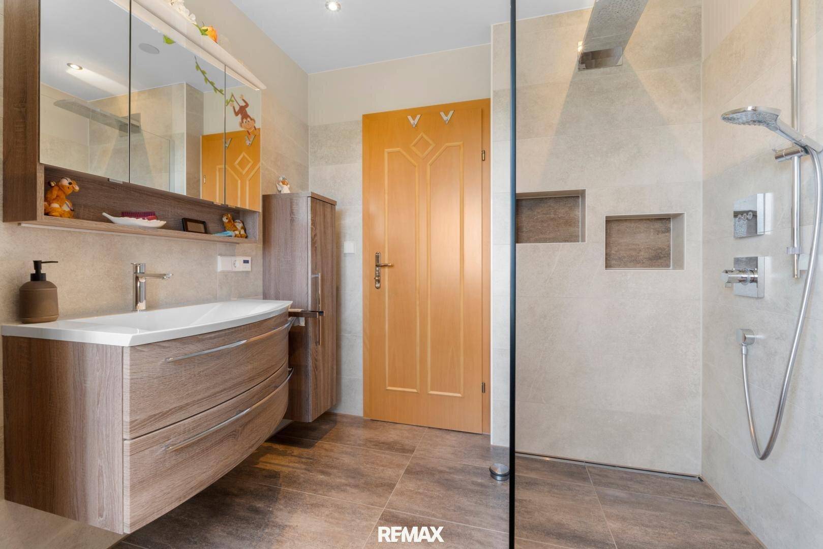 Modernes Badezimmer mit begehbarer Dusche, Waschtischunterschrank und großformatigen Fliesen.