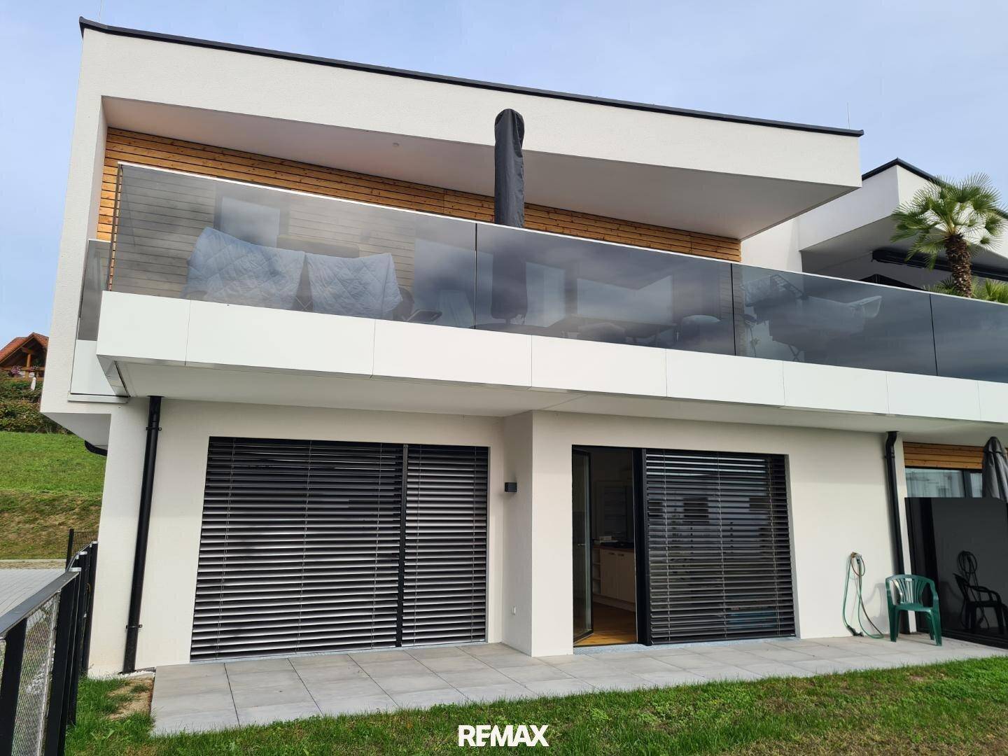 Moderne Architektur mit einer Terrasse im Erdgeschoss und einem Balkon mit Glasgeländer.