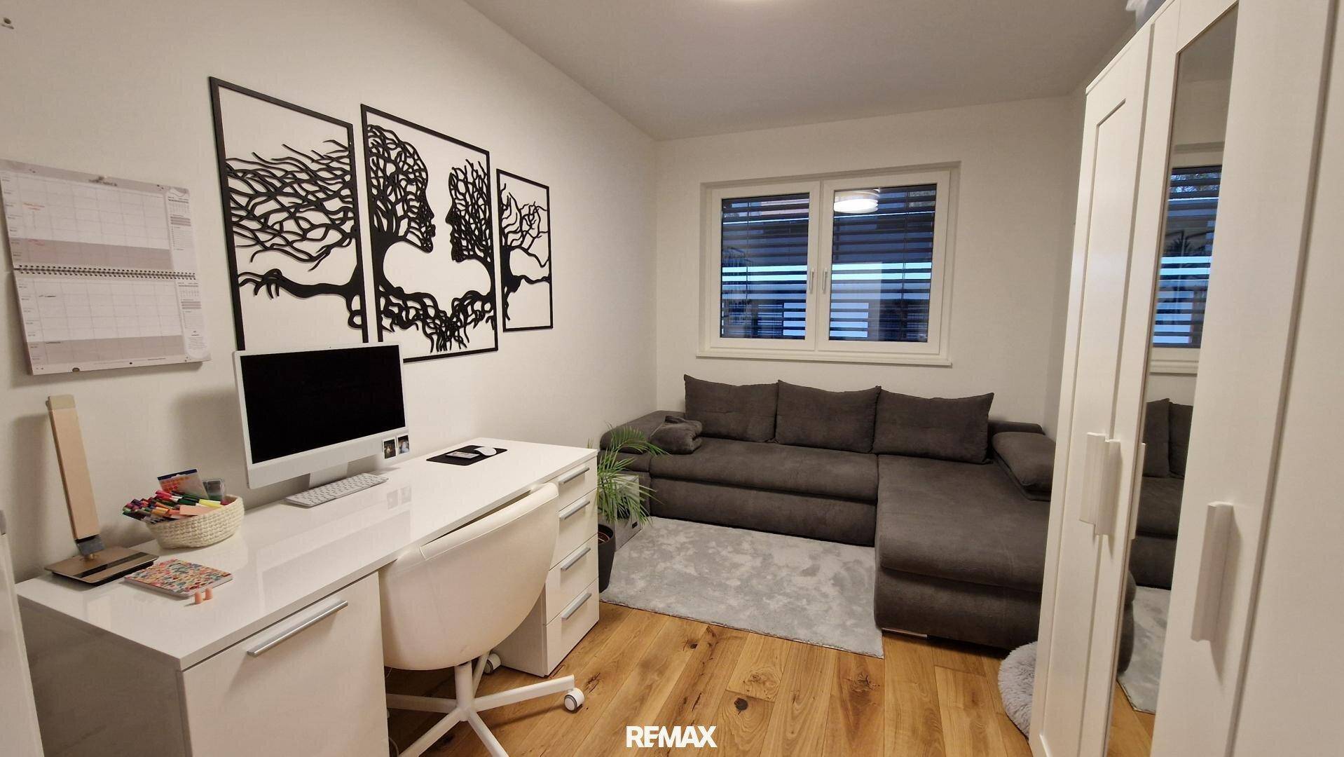 Funktionales Büro oder Gästezimmer mit Schreibtisch, Sofa und Holzboden.