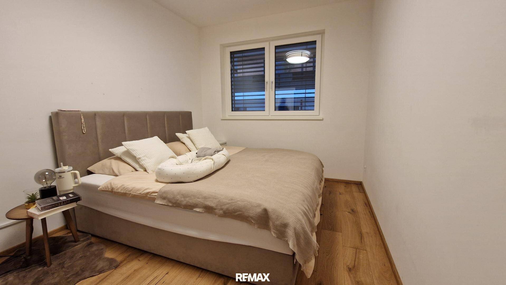 Helles Schlafzimmer mit Doppelbett, Nachttisch und Fenster mit Jalousien.