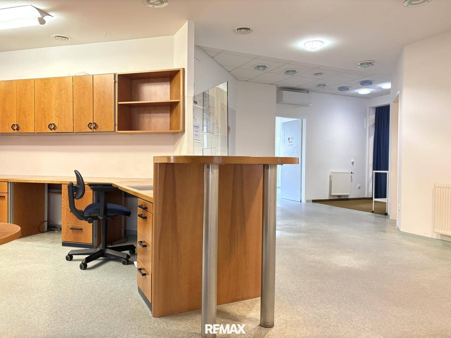Nahaufnahme eines Bürobereichs mit Holzschränken, Schreibtisch und einem Empfangstresen in einem gewerblichen Raum.