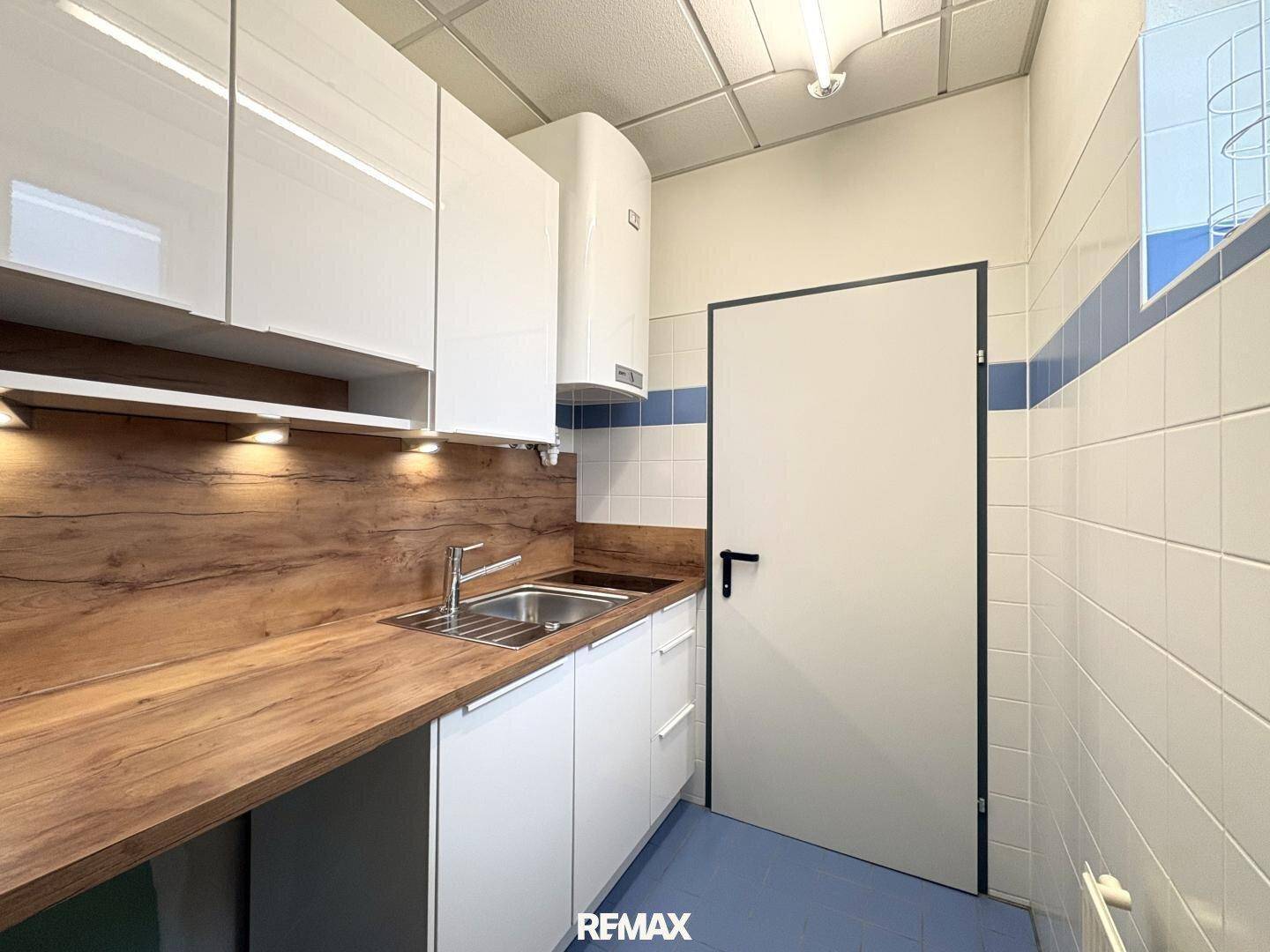 Kleine Küche mit weißen Hochglanzschränken, Holztheke und Edelstahlspüle in einem funktionalen Design.