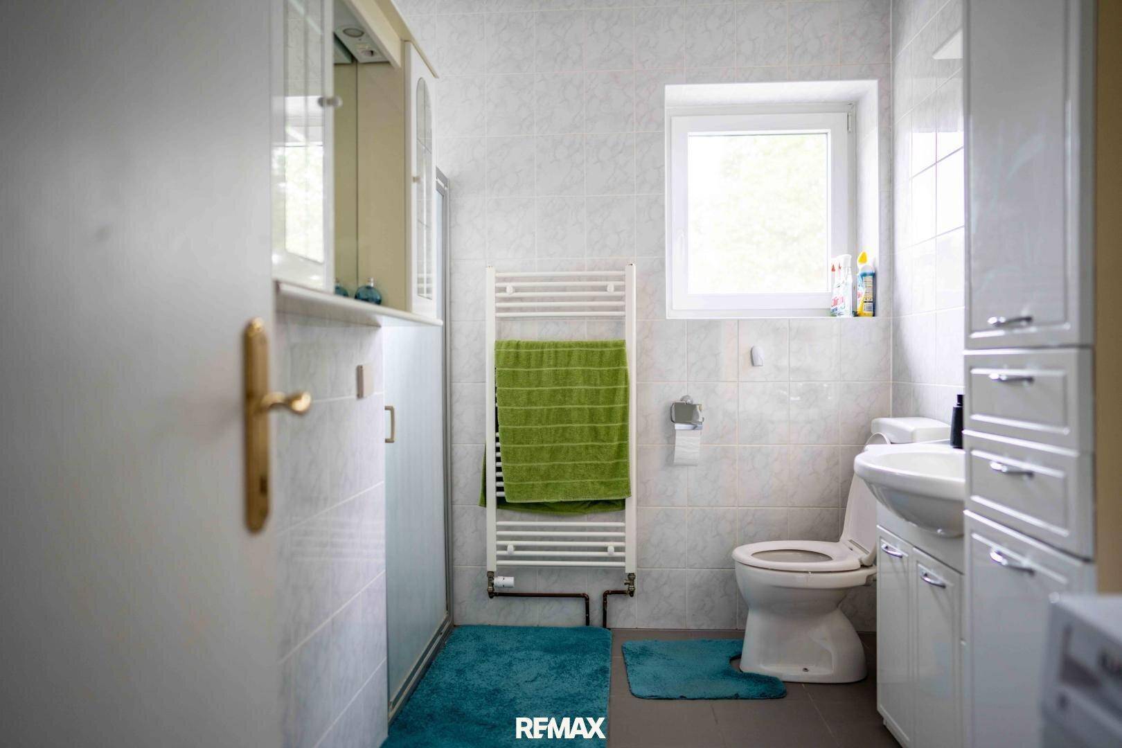 Modernes Badezimmer mit Dusche, WC, Fenster und beheiztem Handtuchhalter.
