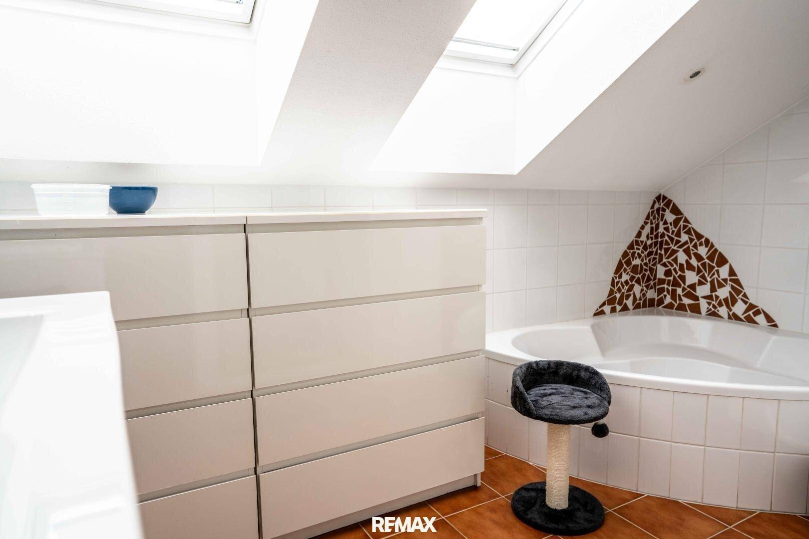 Badezimmer im Dachgeschoss mit Eckbadewanne, Dachfenstern und Terrakotta-Fliesenboden.