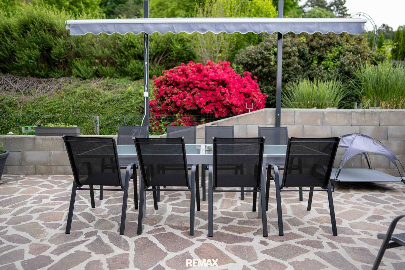 Gemütliche Terrasse mit großem Esstisch und Stühlen, umgeben von üppiger Bepflanzung.