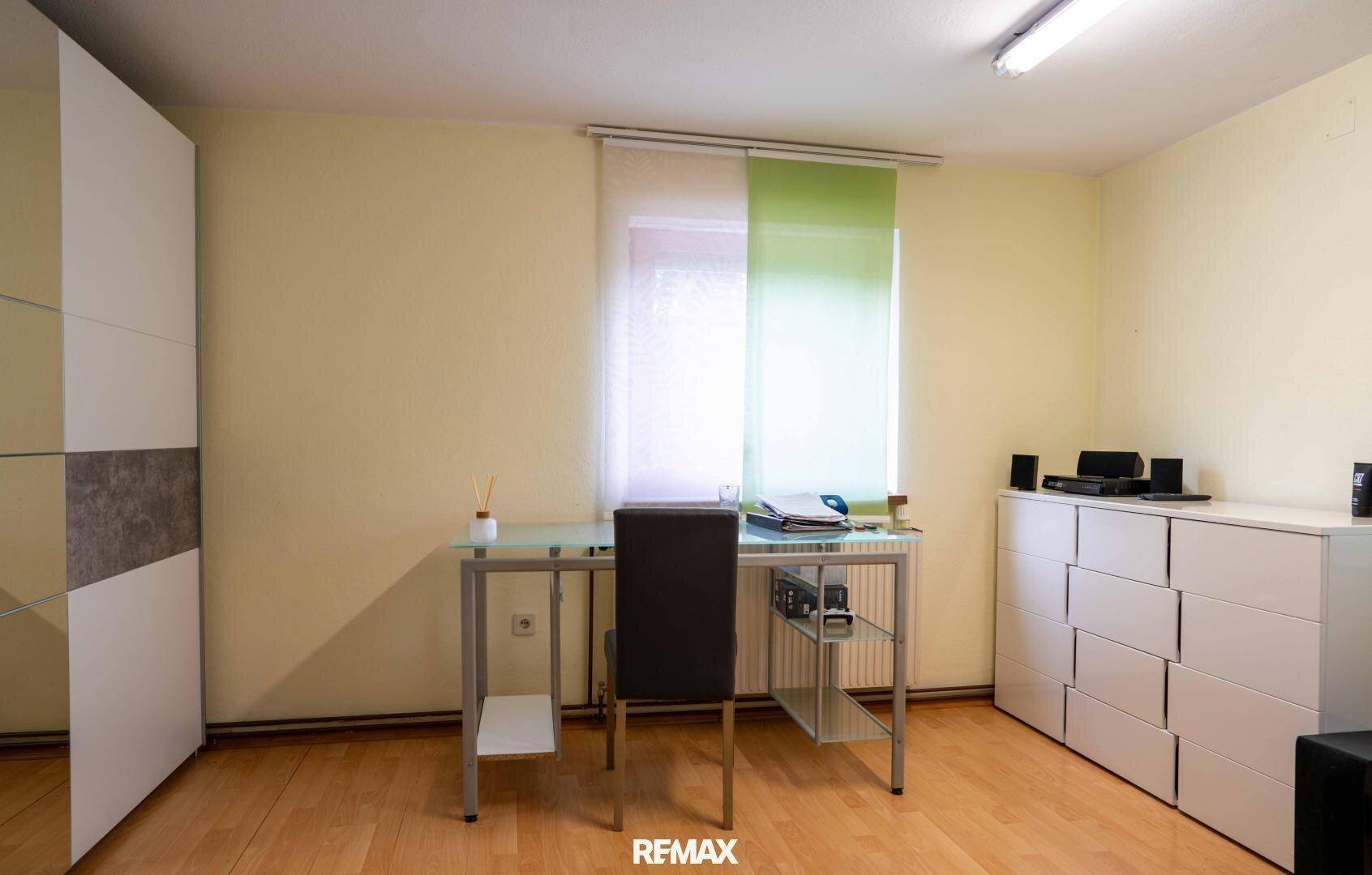 Helles Arbeitszimmer mit Schreibtisch, Schrank und Holzboden.