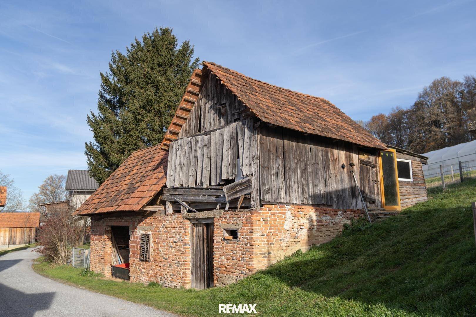 Altes, rustikales Scheunengebäude mit Ziegeldach und verwitterter Holzfassade in ländlicher Umgebung.