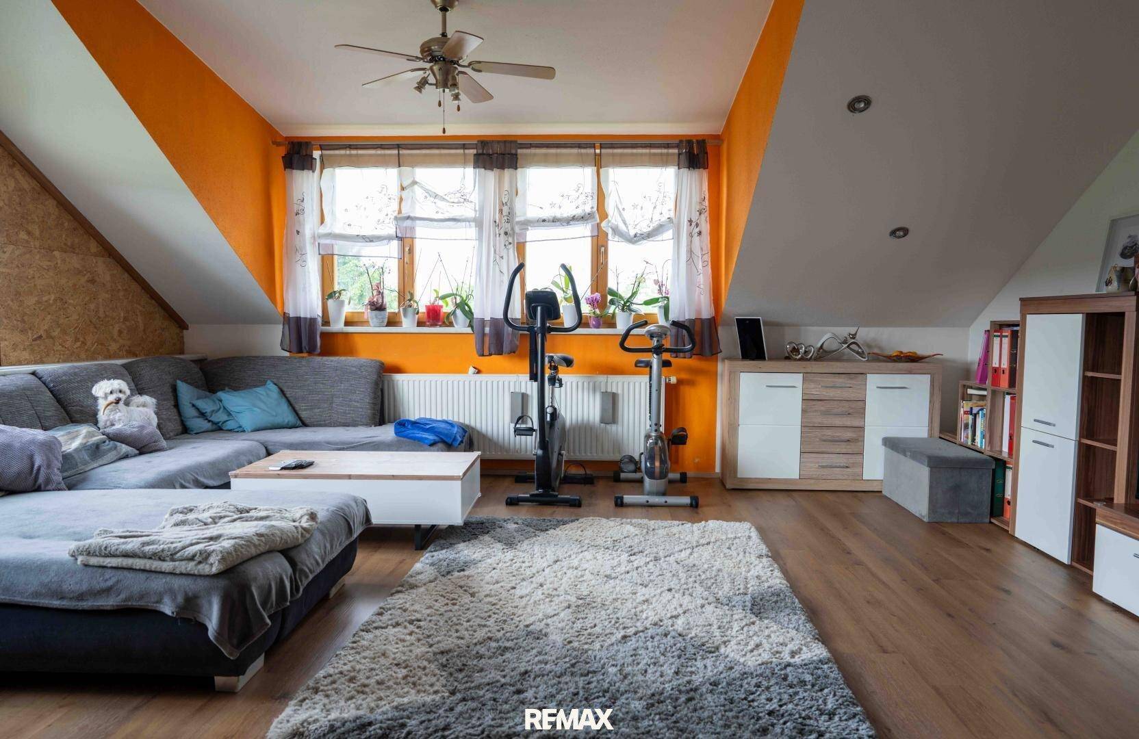 Geräumiges Wohnzimmer im Dachgeschoss mit orangefarbenen Wänden, Sofa und Fitnessgeräten.