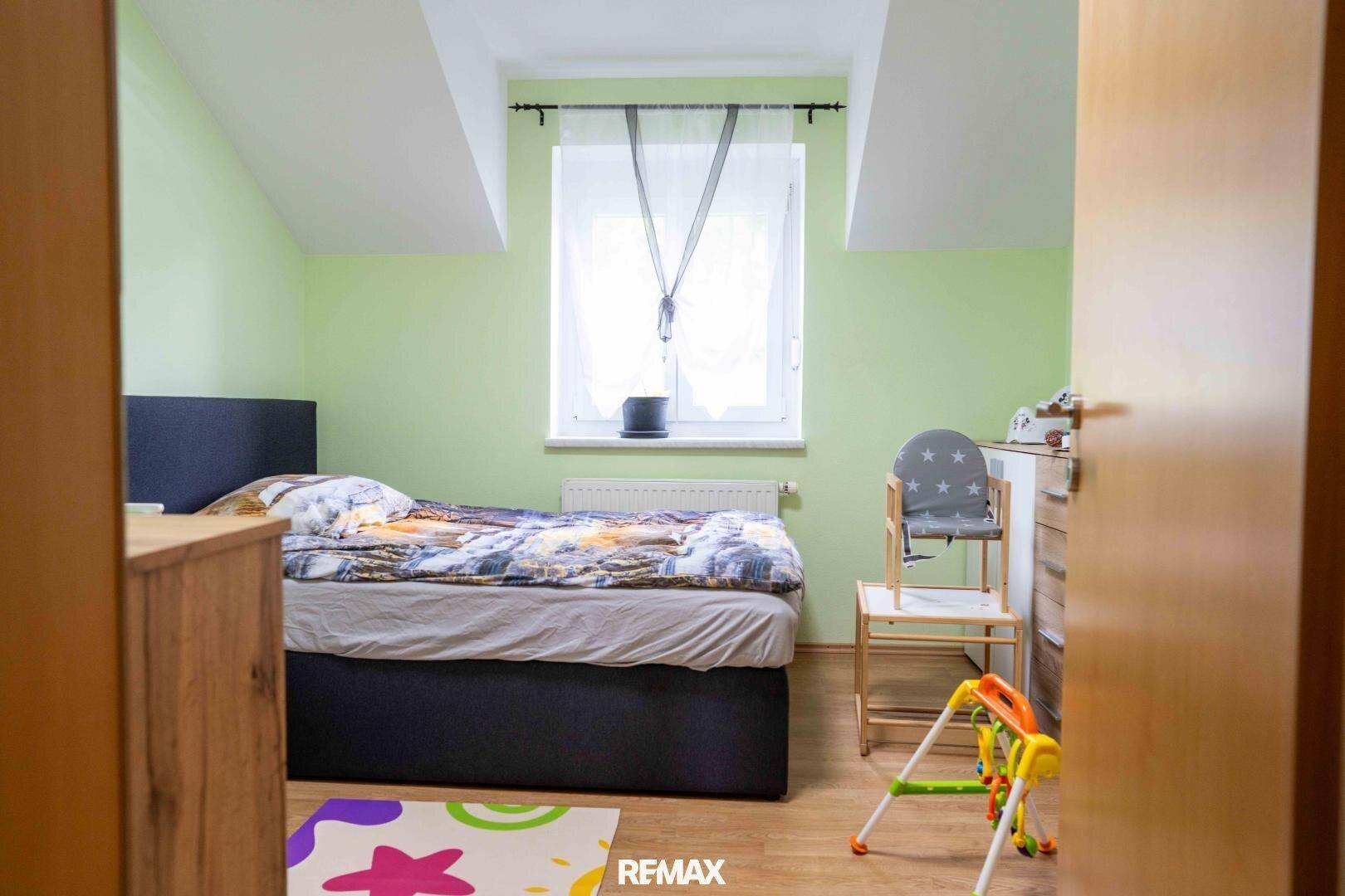 Kinderzimmer im Dachgeschoss mit hellem Holzboden, grünen Wänden und Fenster.