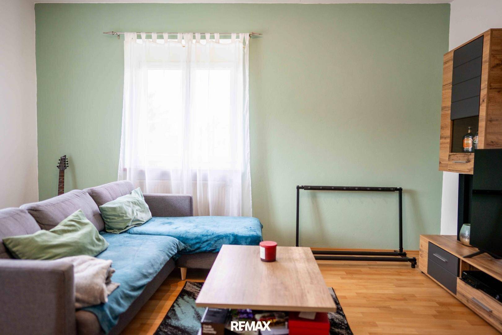 Gemütliches Wohnzimmer mit Sofa, Holzboden und hellgrüner Akzentwand.