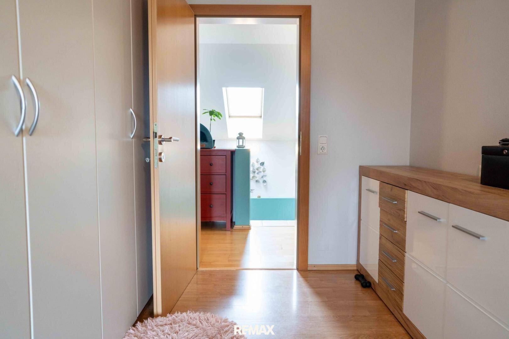 Heller Flur mit Holzboden und Blick in ein angrenzendes Zimmer mit Dachfenster.