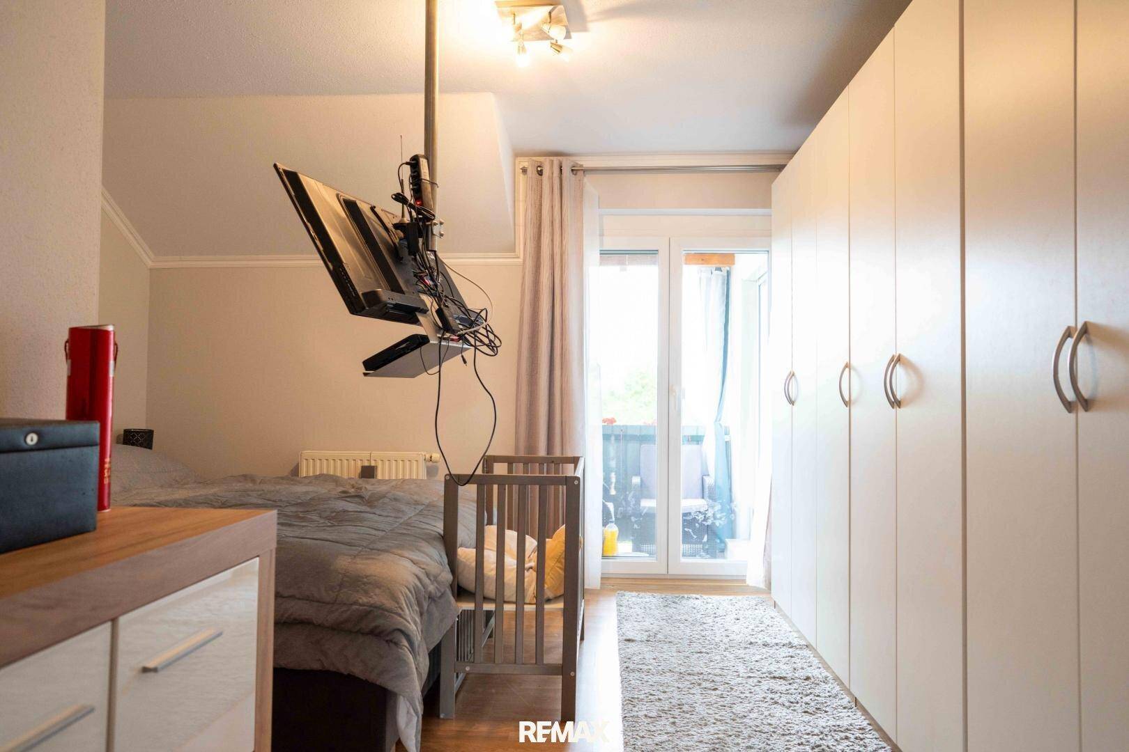 Schlafzimmer mit Einbauschränken, Babybett und Zugang zu einem Balkon.