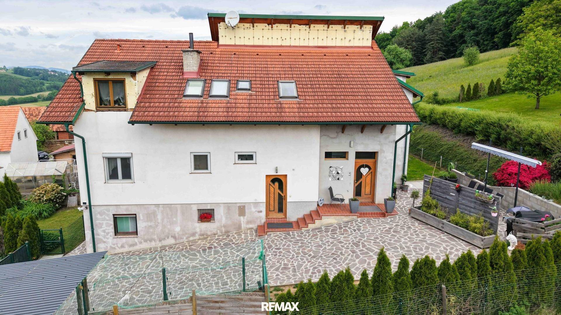 Vorderansicht des Hauses mit zwei Eingängen, gepflastertem Vorplatz und gepflegter Hecke.