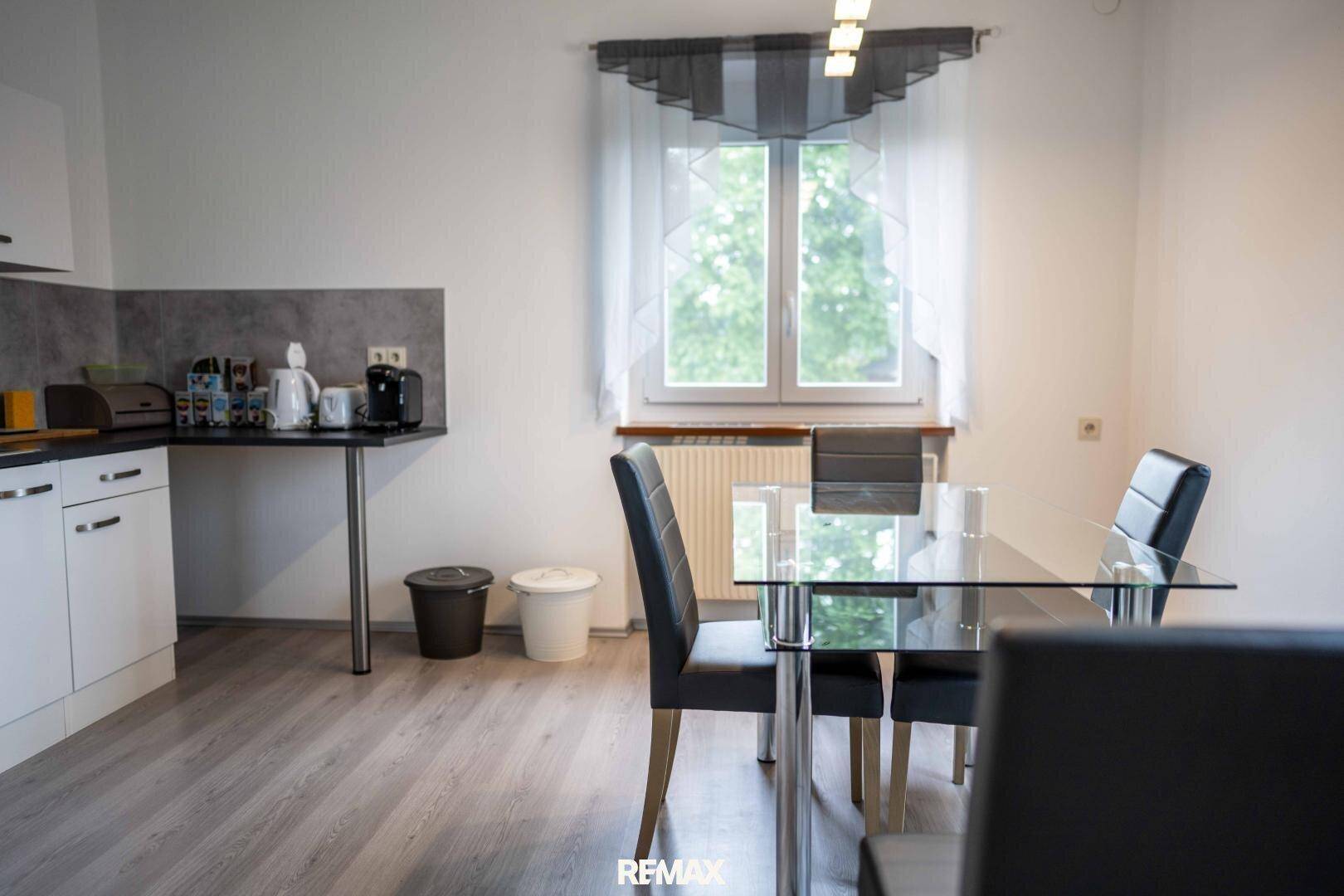 Moderne Küche mit Essbereich, hellem Laminatboden und Blick ins Grüne.