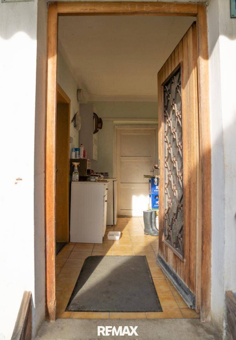 Heller Eingangsbereich mit gefliestem Boden und einer offenen Holztür, die in den Innenraum führt.