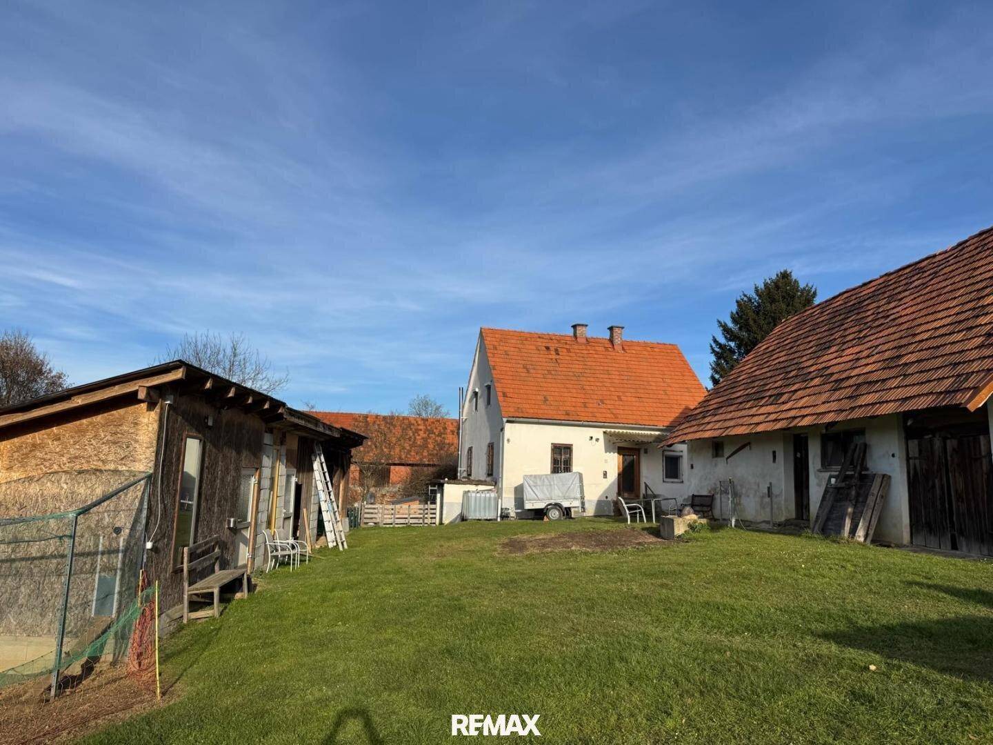 Ländliches Anwesen mit einem Wohnhaus und mehreren Nebengebäuden, umgeben von einer großen Rasenfläche und Bäumen.