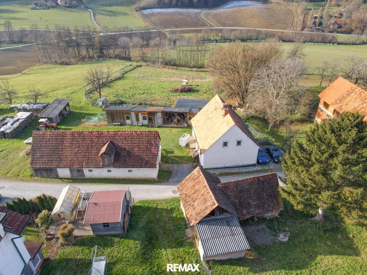 Luftaufnahme von mehreren ländlichen Gebäuden mit roten Ziegeldächern und umliegenden Feldern in herbstlicher Landschaft.