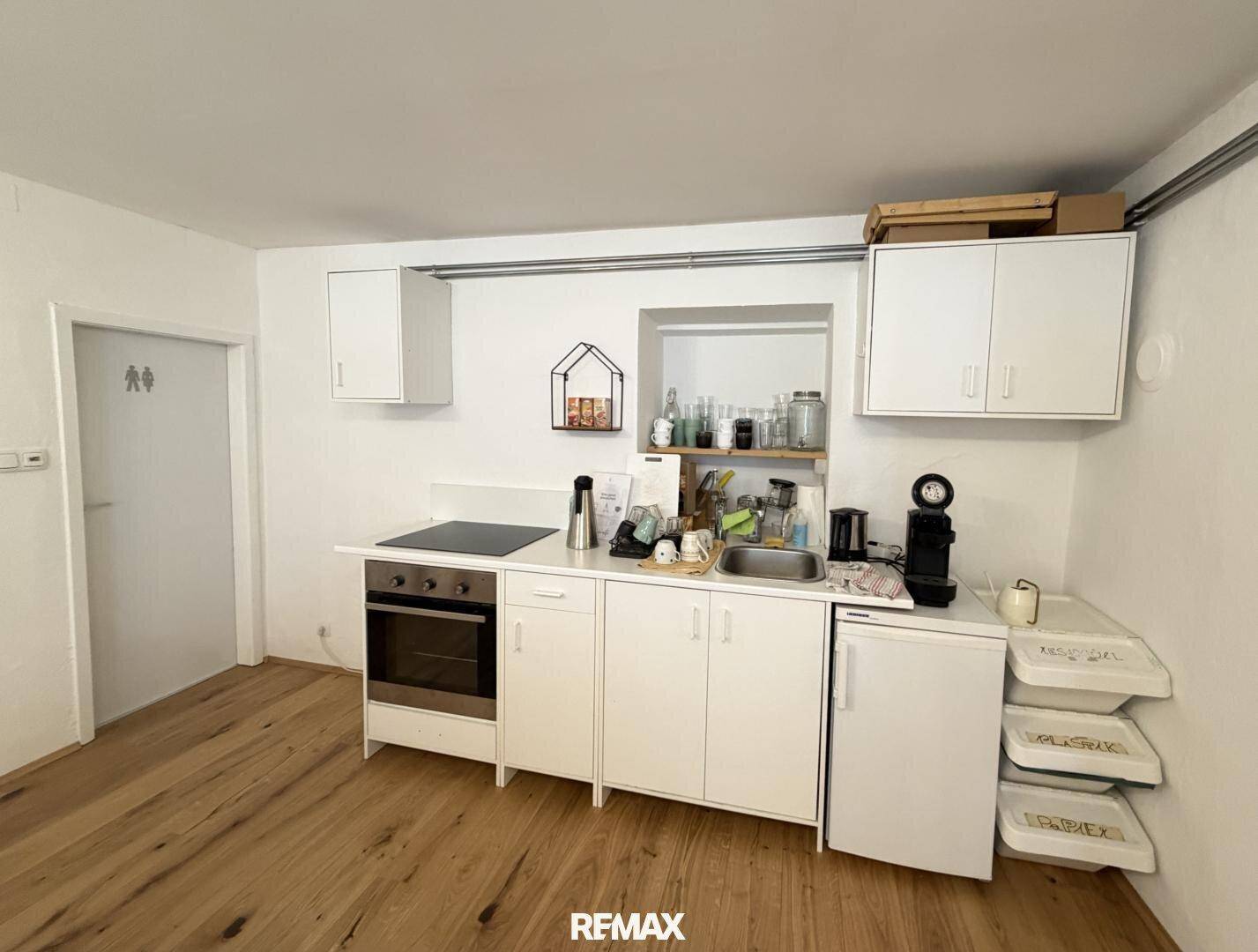 Funktionale Küchenzeile mit weißen Schränken, Kochfeld und Kühlschrank, ideal für kleine Büros.