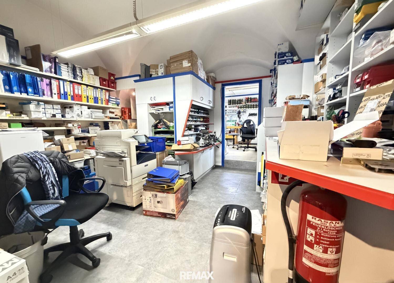 Lagerraum oder Büro-Hinterzimmer mit Regalen, Akten und einem Feuerlöscher.