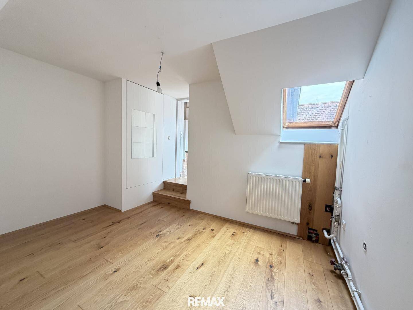 Heller Dachbodenraum mit Holzboden, Dachfenster und einer kleinen Treppe.