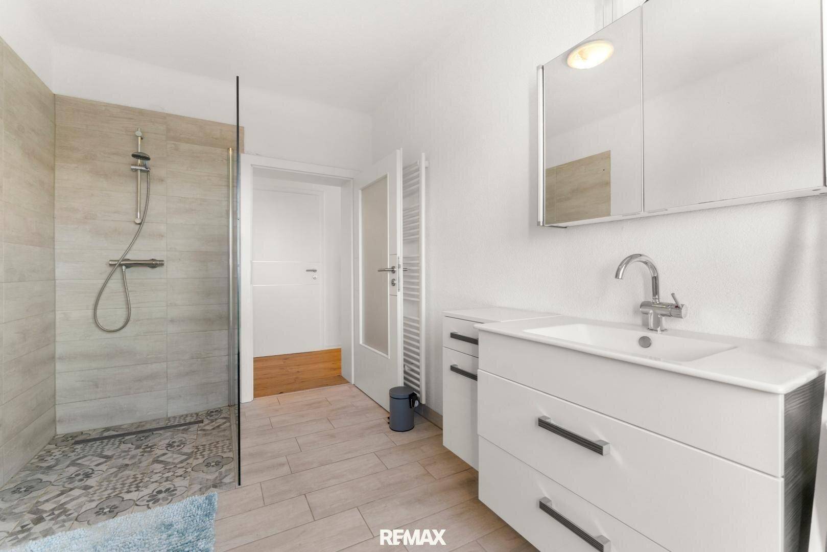 Modernes Badezimmer mit ebenerdiger Dusche, Waschtisch und Spiegelschrank.