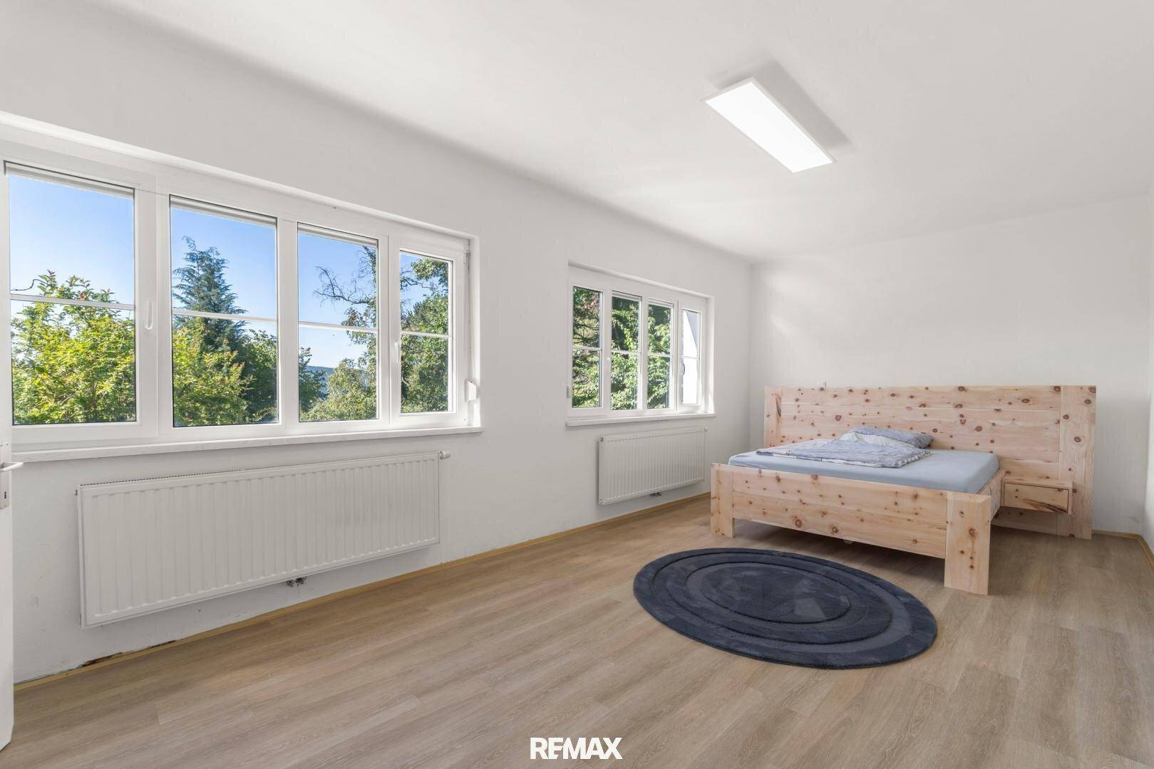 Schlafzimmer mit hellem Holzbett, Holzboden und großen Fenstern mit Ausblick.