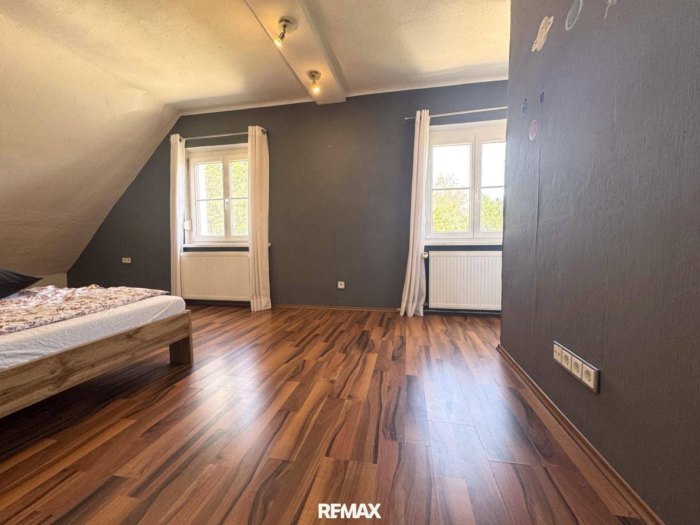 Helles Schlafzimmer mit zwei Fenstern, Holzboden und Dachschrägen.