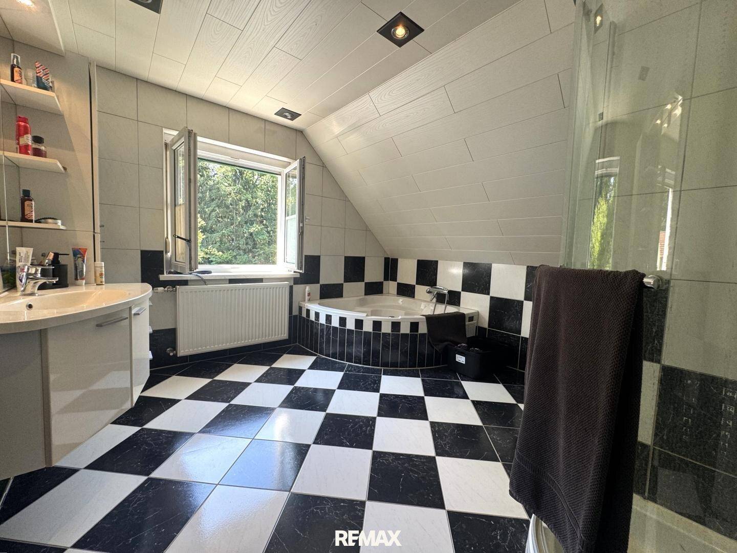 Badezimmer mit schwarz-weiß karierten Fliesen, Eckbadewanne und Dusche.