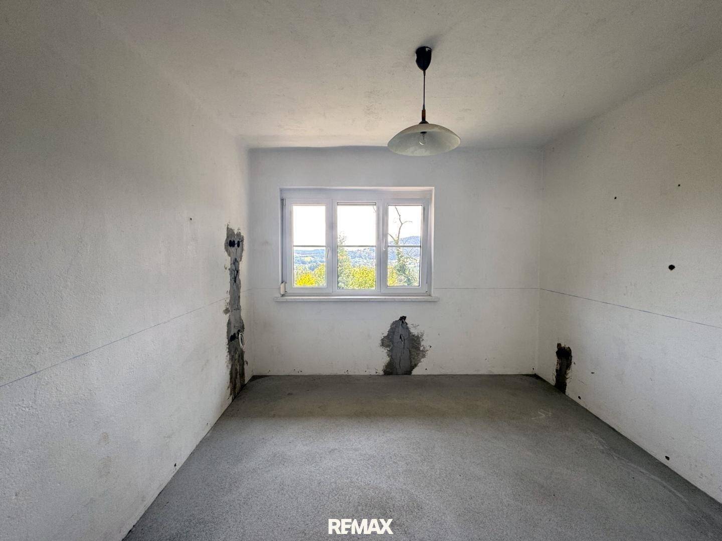Leerer Raum im Rohbau mit weiß gestrichenen Wänden und einem Fenster.