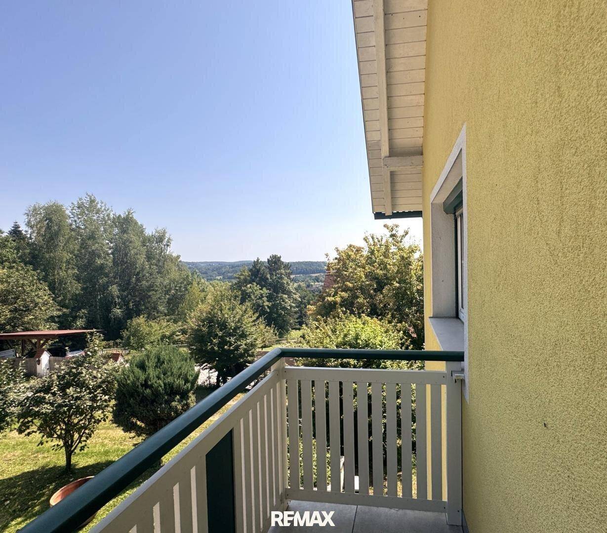 Kleiner Balkon mit Holzgeländer und weitem Blick über die grüne Landschaft.